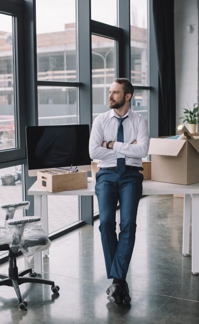 businessman with crossed arms sitting on table and looking away in new office